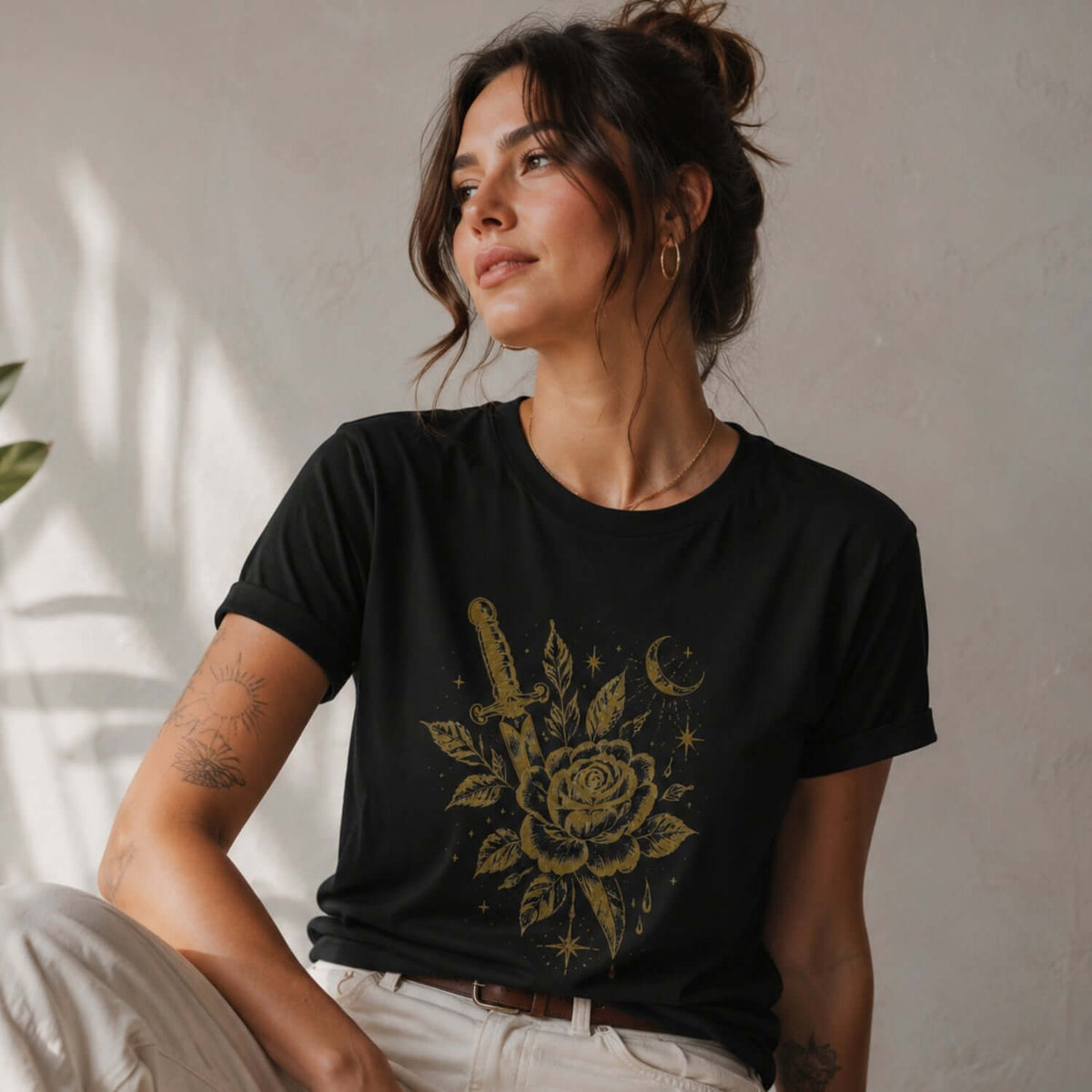 Woman wearing a black dark romantic graphic tee with a gold rose-and-dagger design.